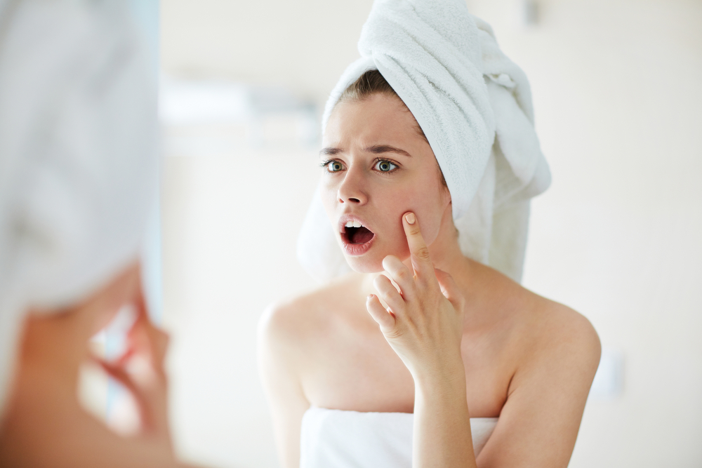 Woman examining pimple on face