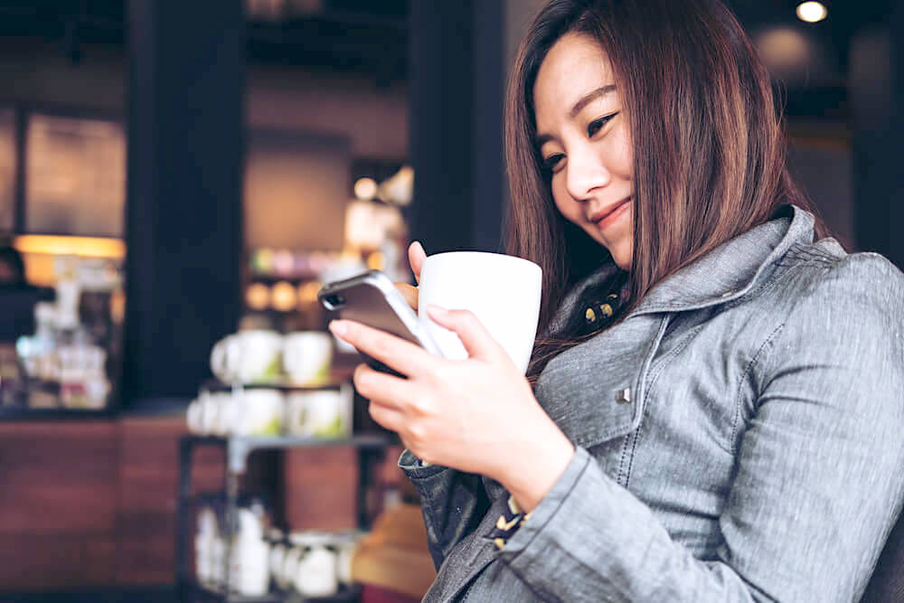 Smiling young woman texting on her phone while enjoying a cup of coffee