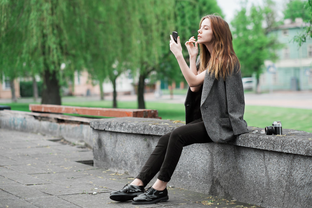 Woman applying lipstick in a park