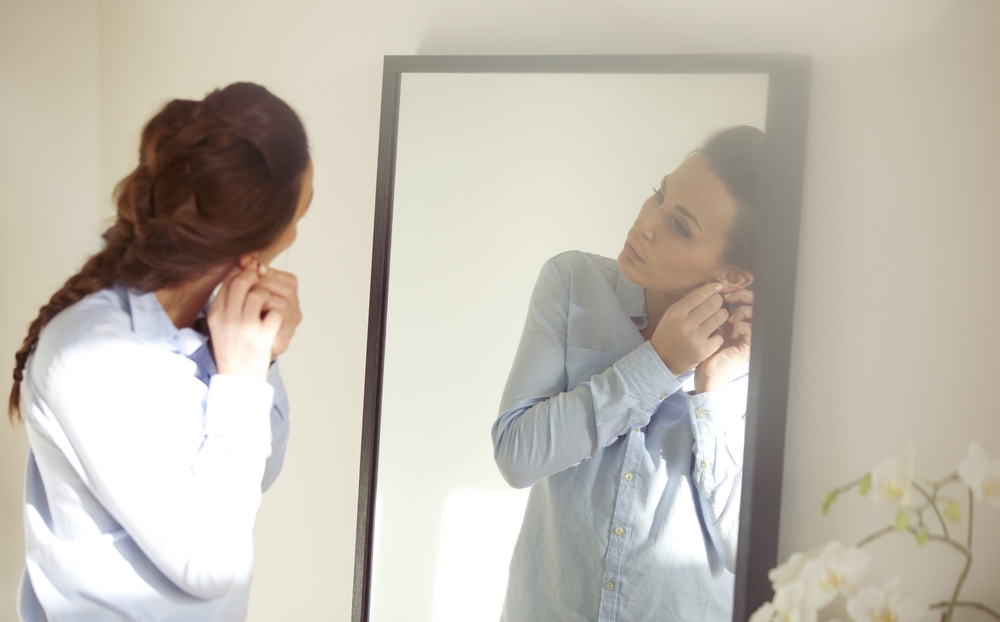 Woman putting on earrings in body-length mirror