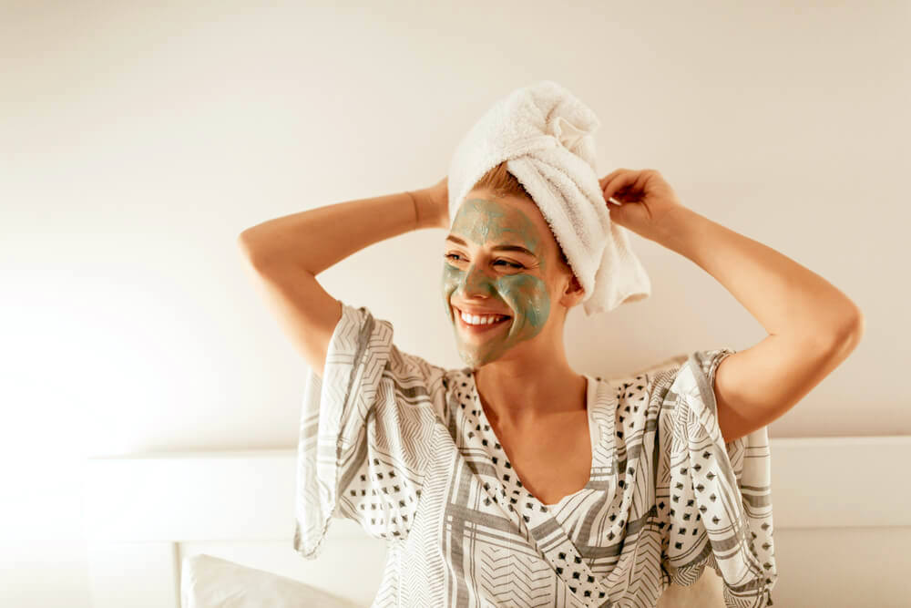 Smiling woman with green face mask and a towel over her hair