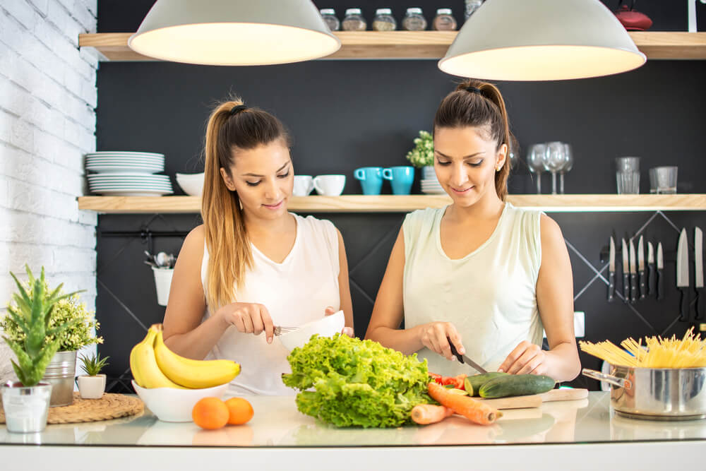 Two female friends making salad in kitchen