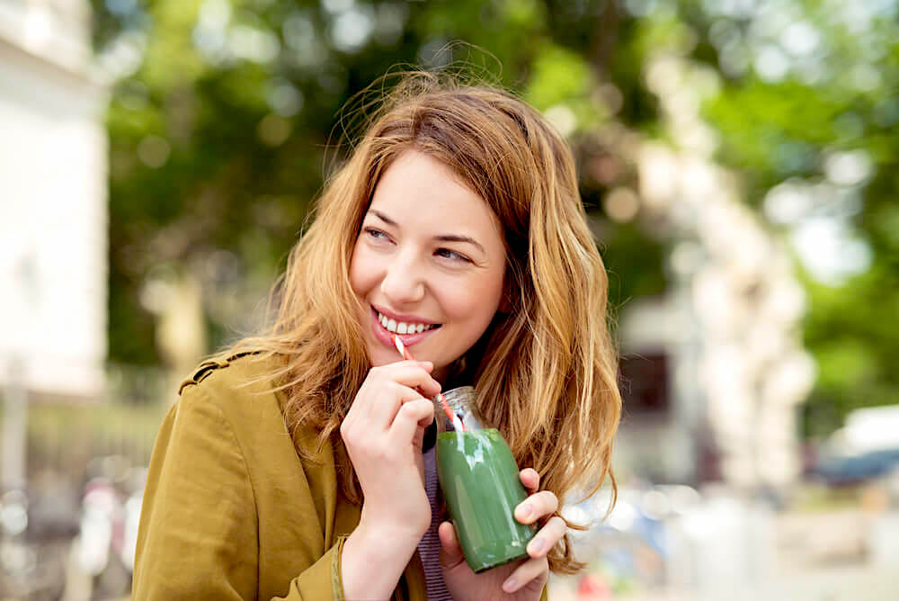 Woman drinking green juice outdoors