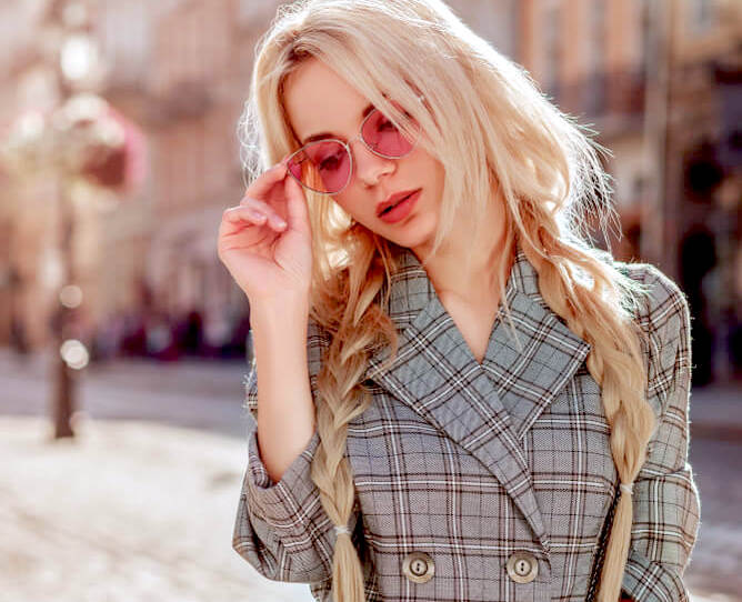 Young blonde woman with rose-tinted sunglasses and loose pigtail braids 