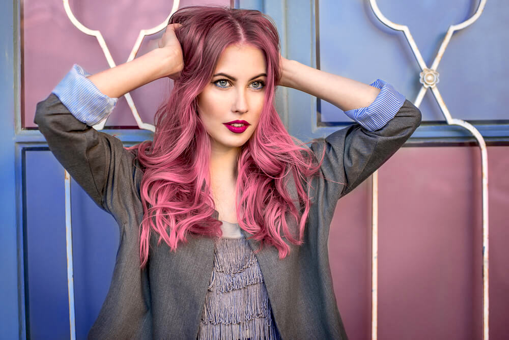 Woman with bright pink curly hair, touching her hair outdoors 