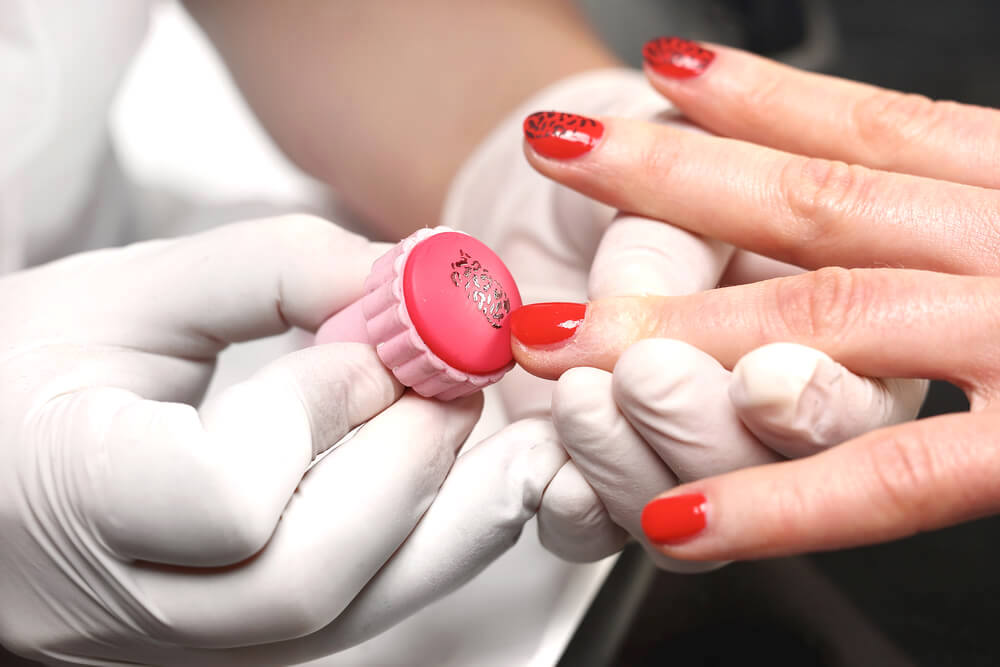 Manicurist applying nail stamp to woman's nails
