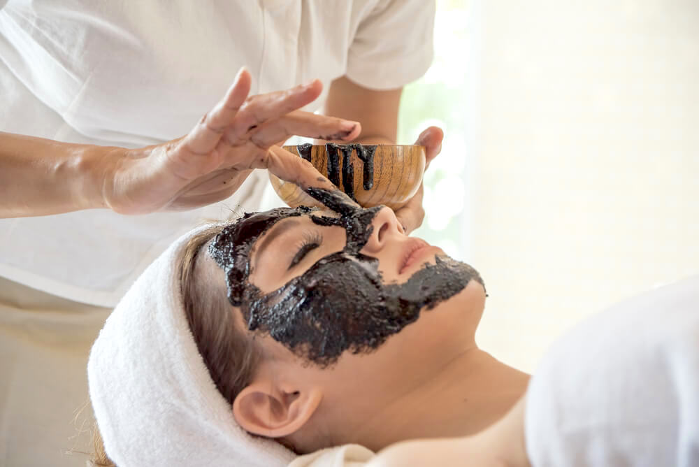 Woman enjoying charcoal facial mask in spa