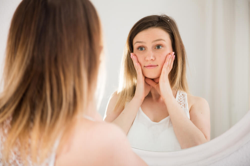 Young woman touching face in front of mirror