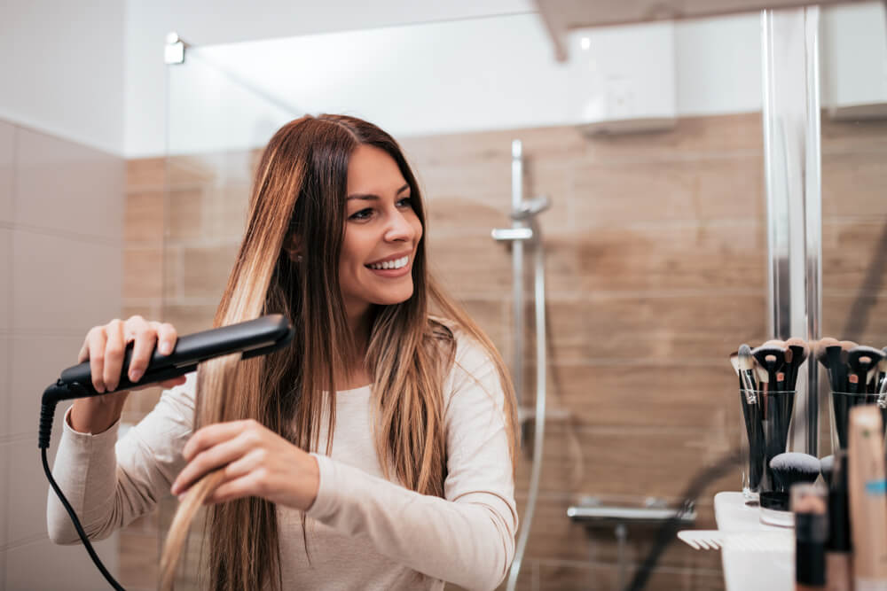 Smiling woman using hair straightener in the bathroom