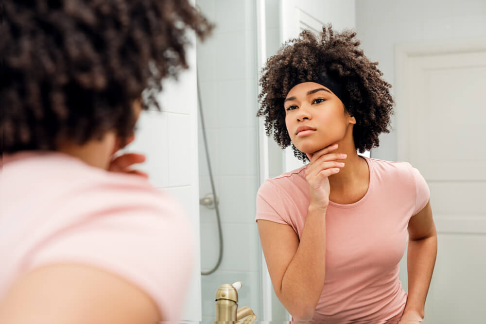 Woman touching her face in front of bathroom mirror