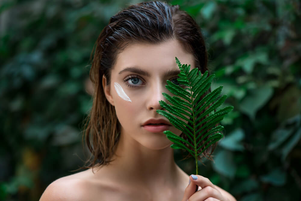 Woman with cream on face and leaf in front of eye