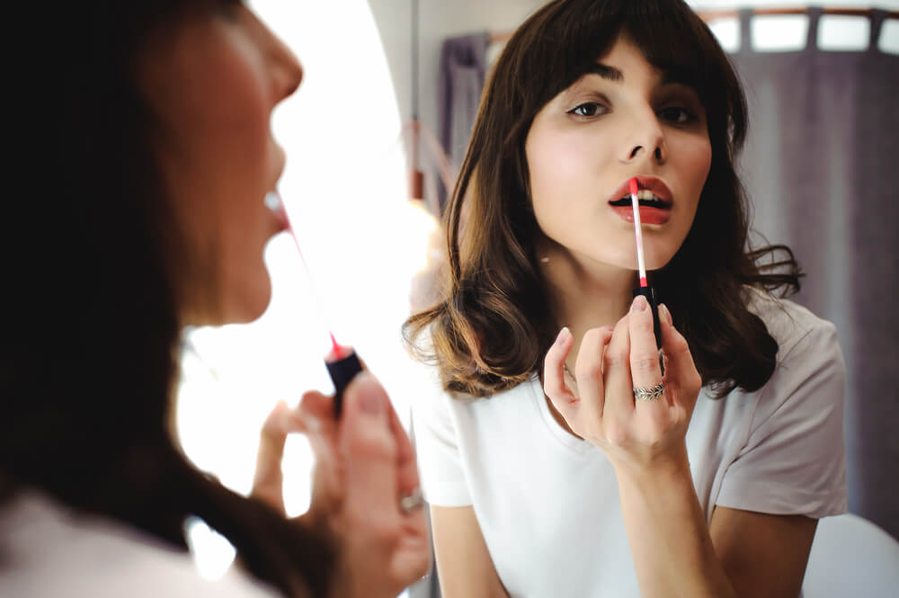 Woman applying lipstick in front of mirror