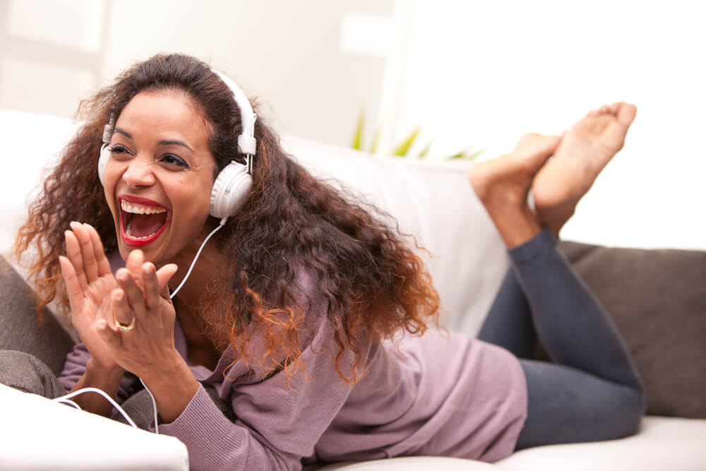 Woman lying on sofa with headphones on looking happy