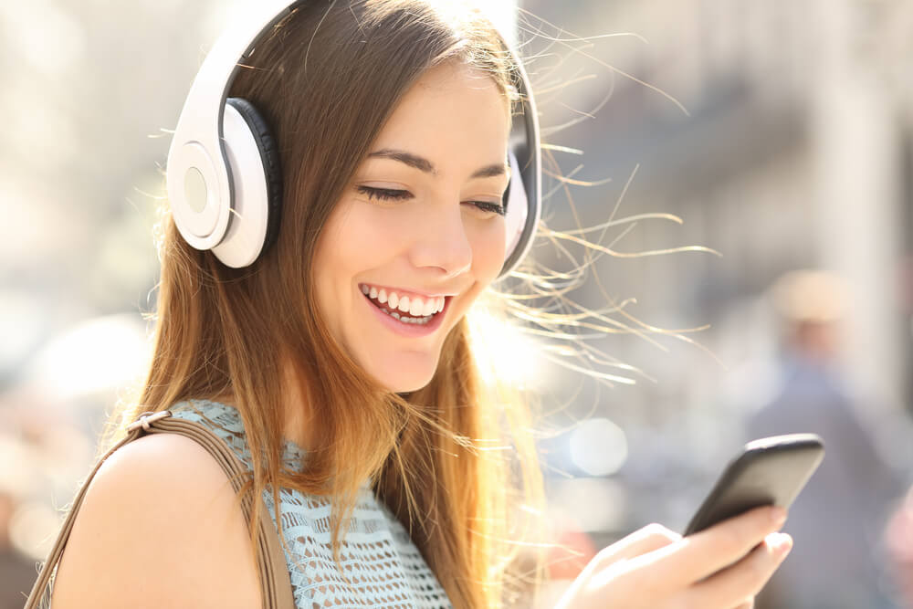 Woman looking at phone with headphones on and smiling