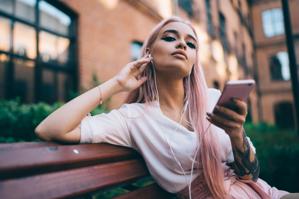 Fashionable woman holding phone with headphones in ears