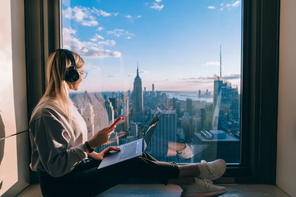 Woman with laptop and headphones by window