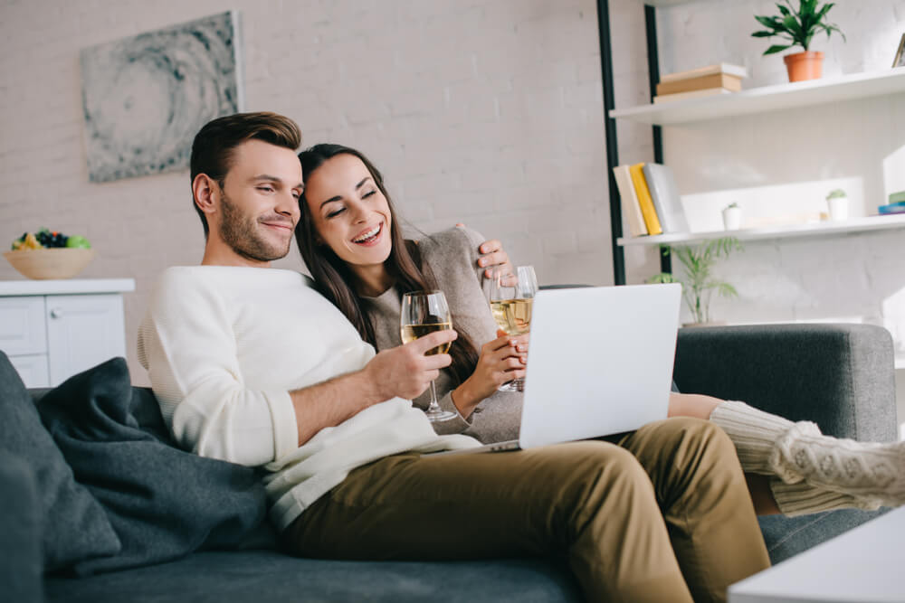 Couple with wine laughing at laptop